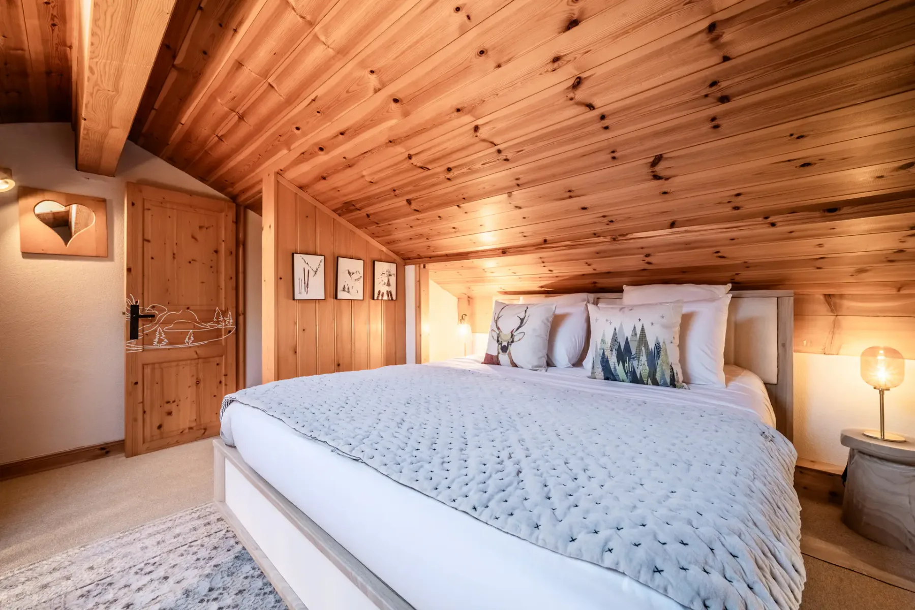 Cozy attic bedroom with wooden ceiling, double bed, round mirror on a white dresser, and a bedside lamp.