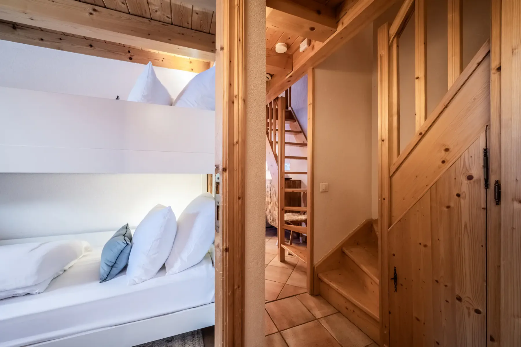 A wooden interior features a bunk bed to the left, a wooden staircase on the right, and a tiled floor.