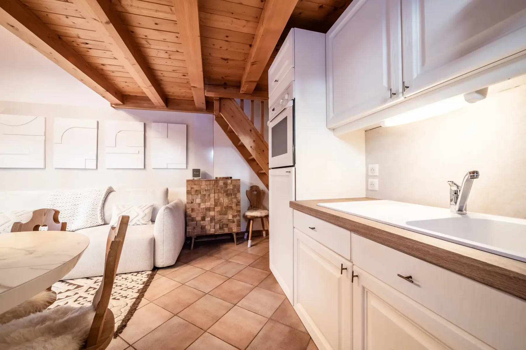 Wood-paneled kitchen with white cabinets, a small white shelf holding kitchen appliances, and a dining table with wooden chairs. A large window shows a snowy landscape outside.