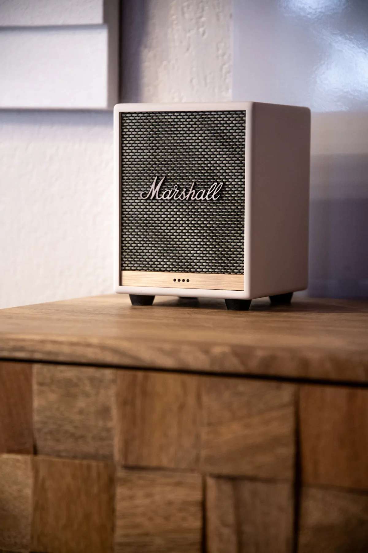 A compact Marshall speaker with a mesh grille sits on a wooden surface.