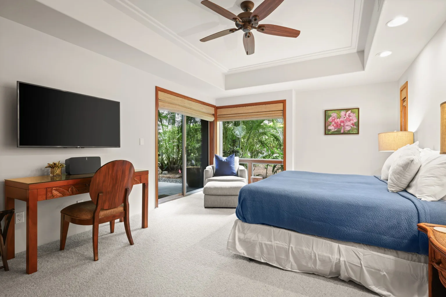 A bedroom with a large bed, a desk, and glass doors opening to greenery.