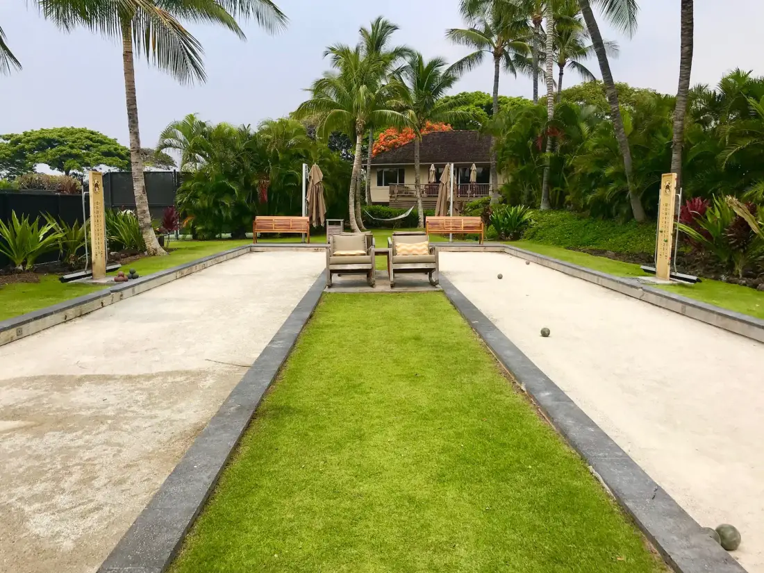 A landscaped outdoor recreation area has a central lawn bordered by two paved courts.