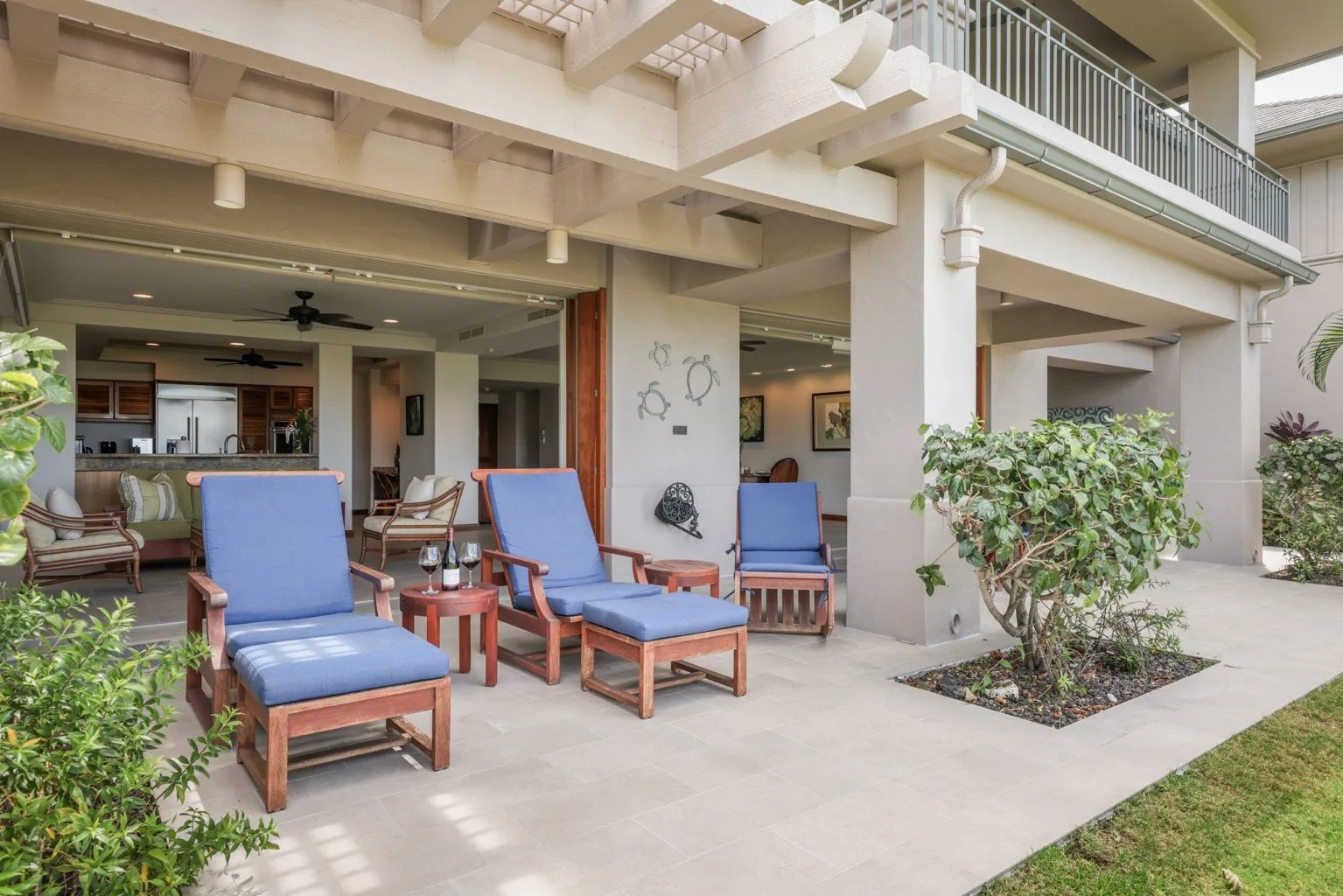 A covered patio with blue-cushioned seating opens onto a landscaped courtyard.