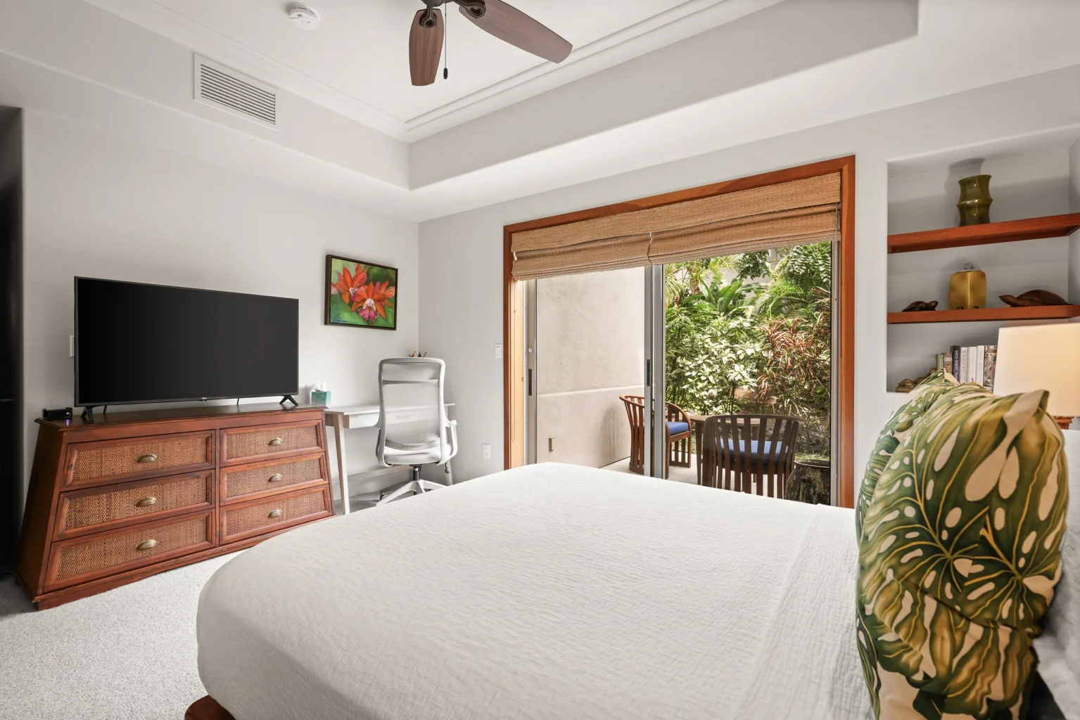 A bright bedroom with a bed, a television, and glass doors opening to greenery.