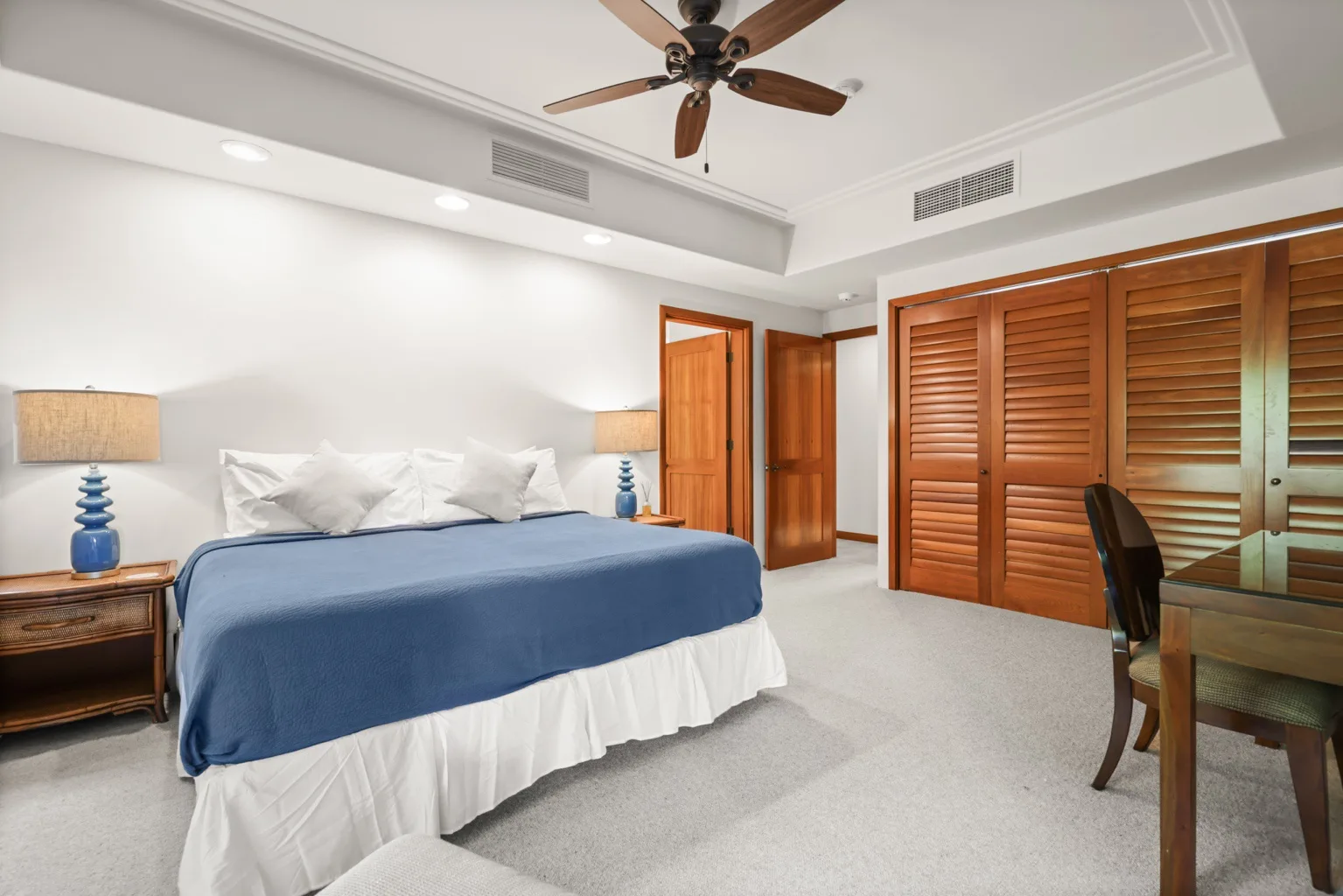 A bedroom with a bed covered in blue bedding and wooden louvered doors.