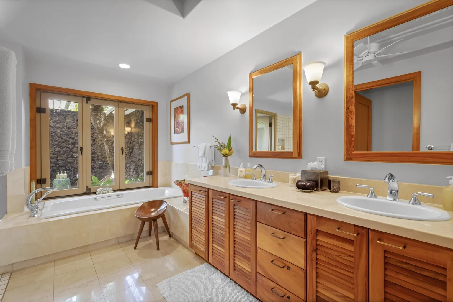 A bright bathroom with a long vanity and a bathtub beside glass doors.