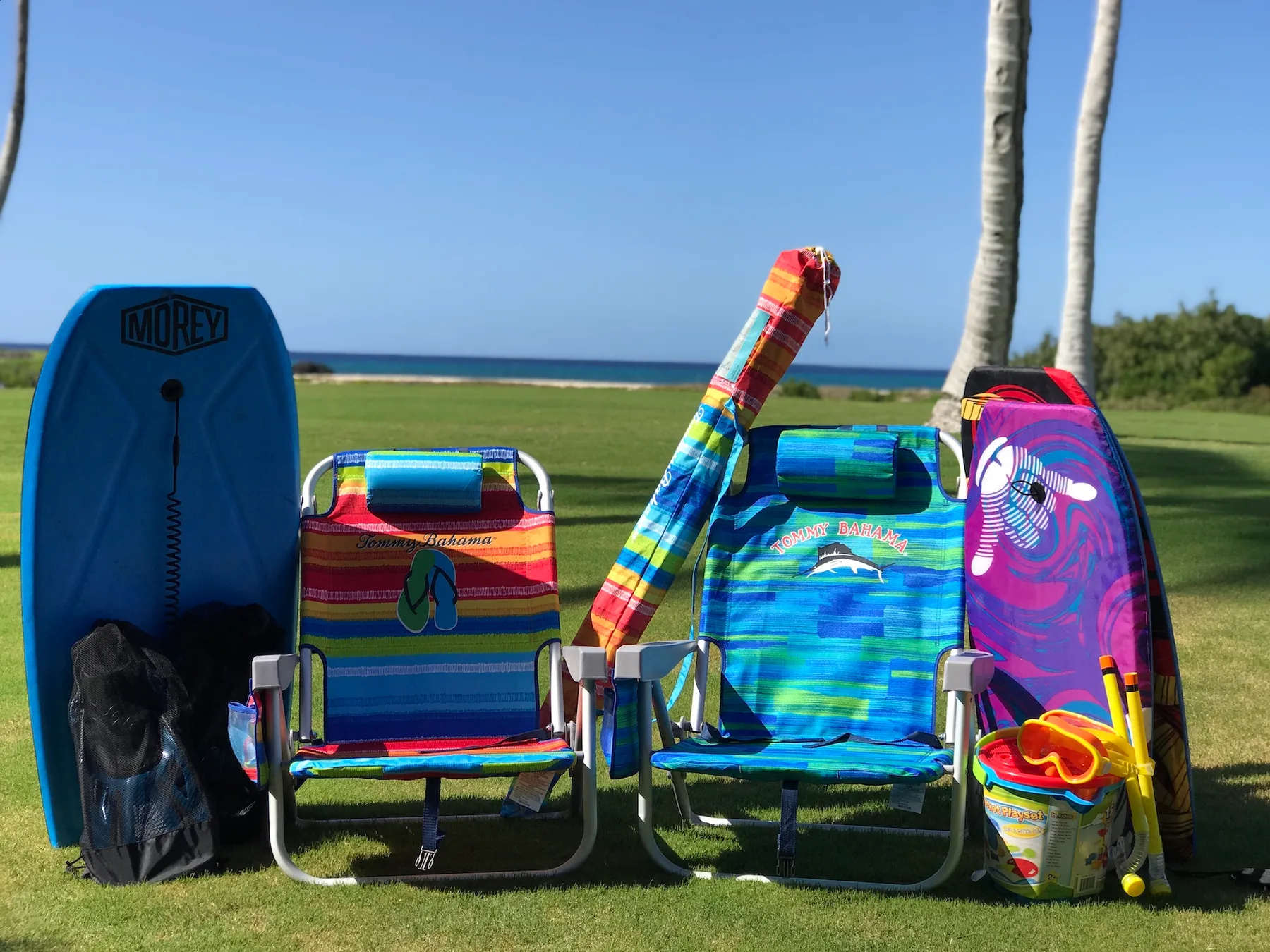 Beach chairs and colorful boards are arranged on a grassy lawn beside the ocean.