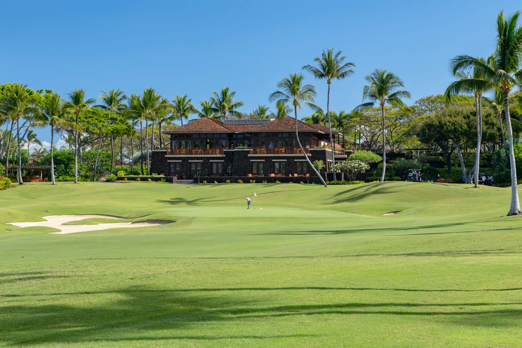 A landscaped golf course with a clubhouse and palm trees.