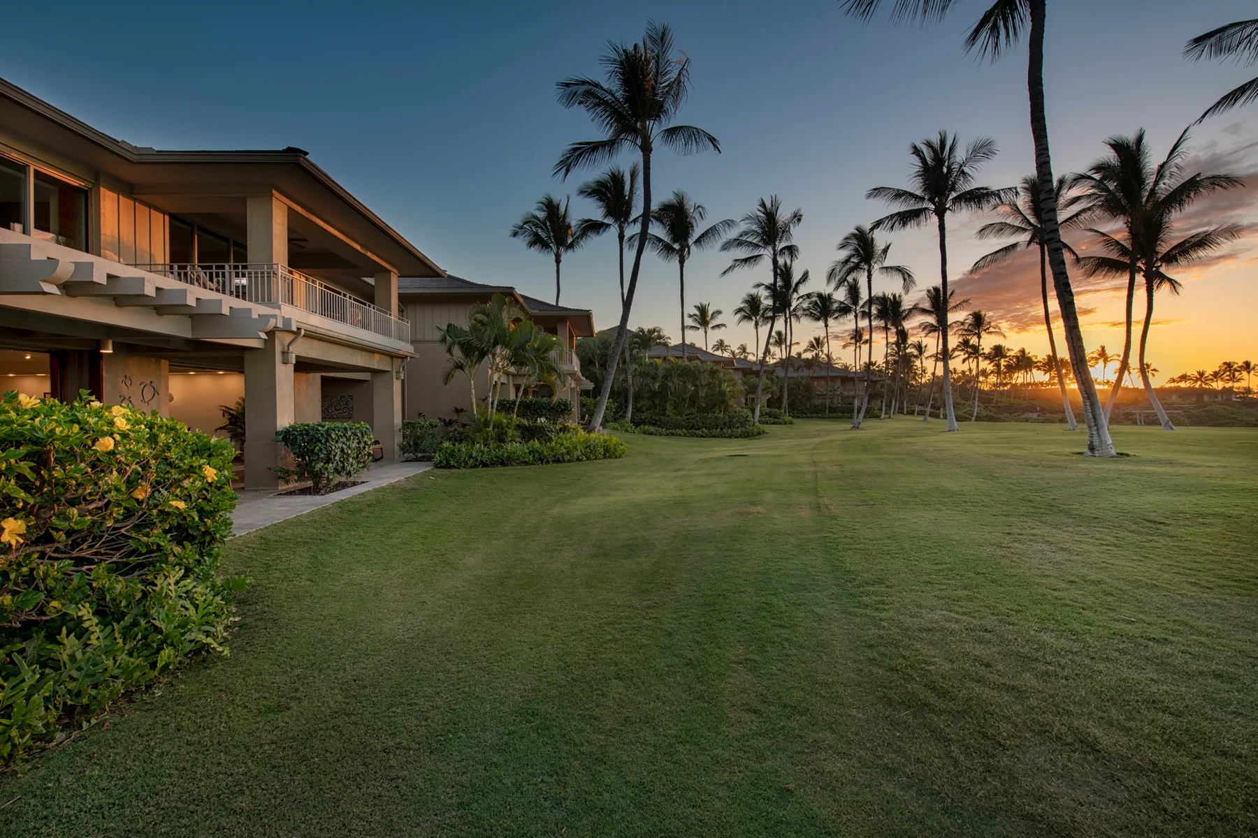 A landscaped lawn beside a low-rise building, with palm trees at sunset.