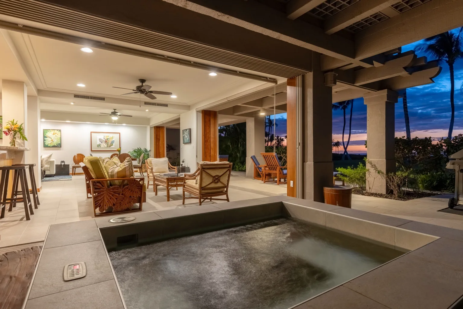 An open-plan living and dining area beside a recessed outdoor pool at dusk.