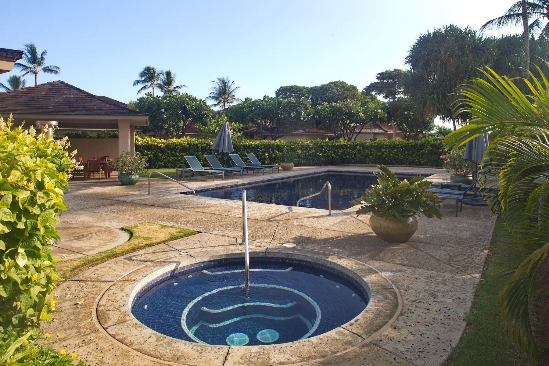 A pool courtyard with a round spa in the foreground and lounge seating nearby.