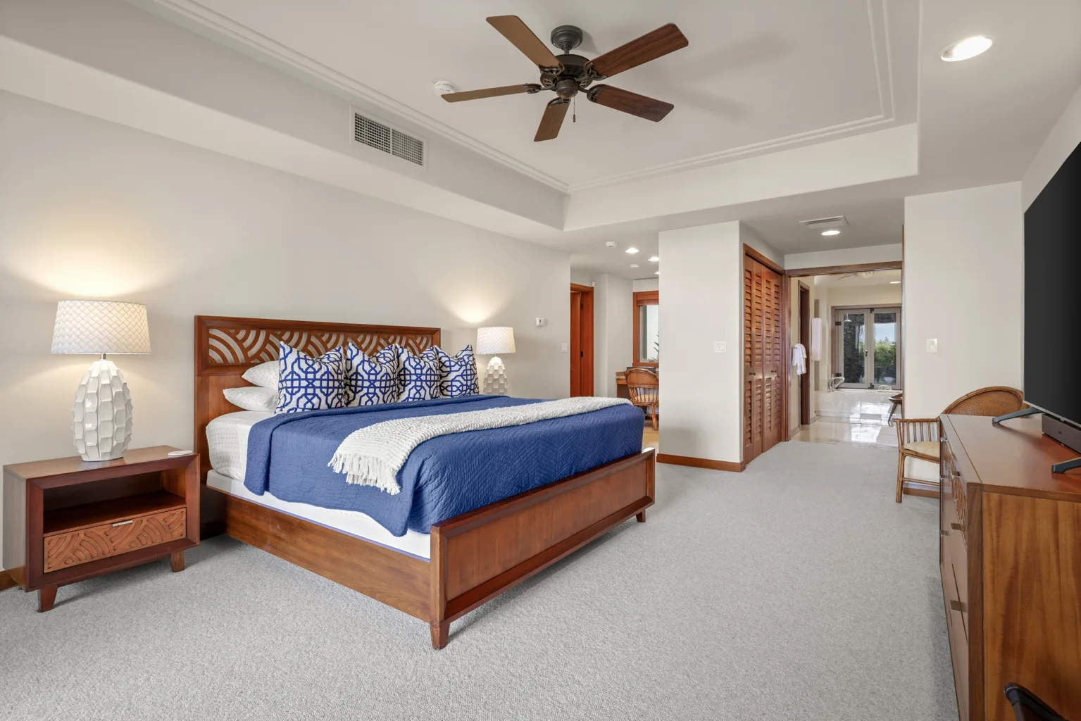 A bright bedroom with a wooden bed, blue bedding, and a ceiling fan.