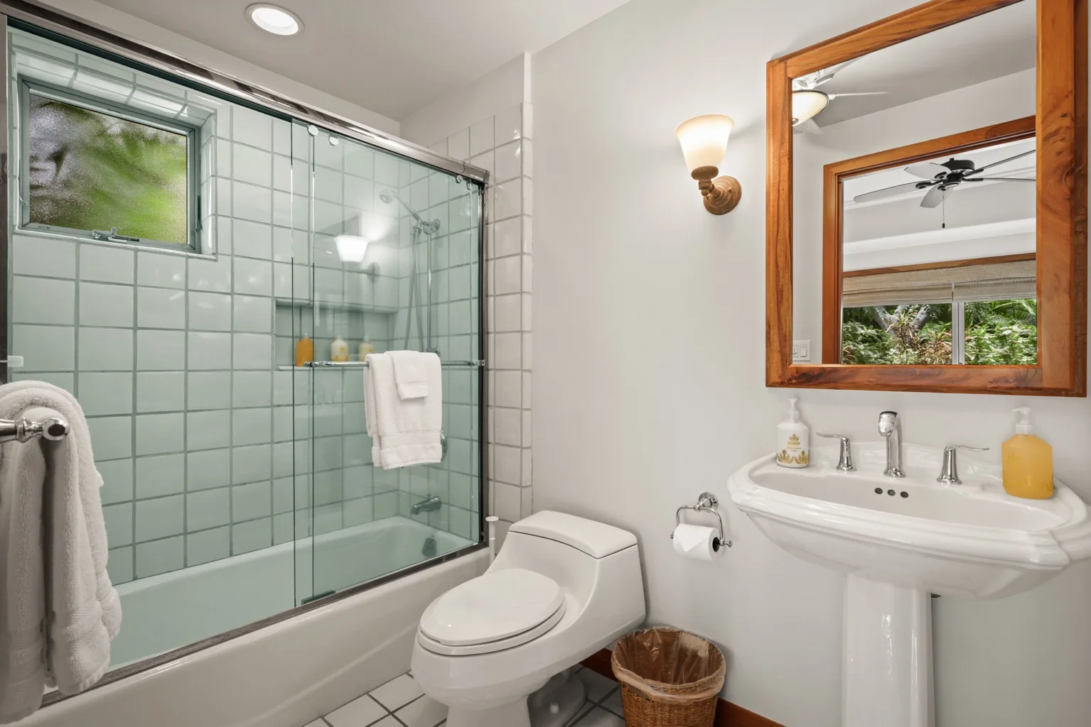A bathroom with a glass-paneled shower, toilet, and pedestal sink.