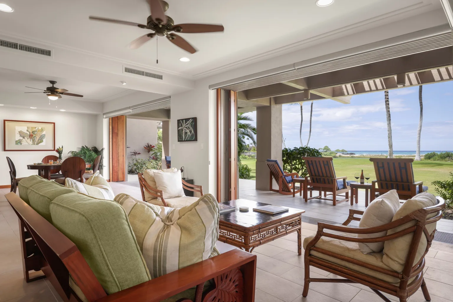 A bright living room opens onto a covered patio with seating and ocean views.