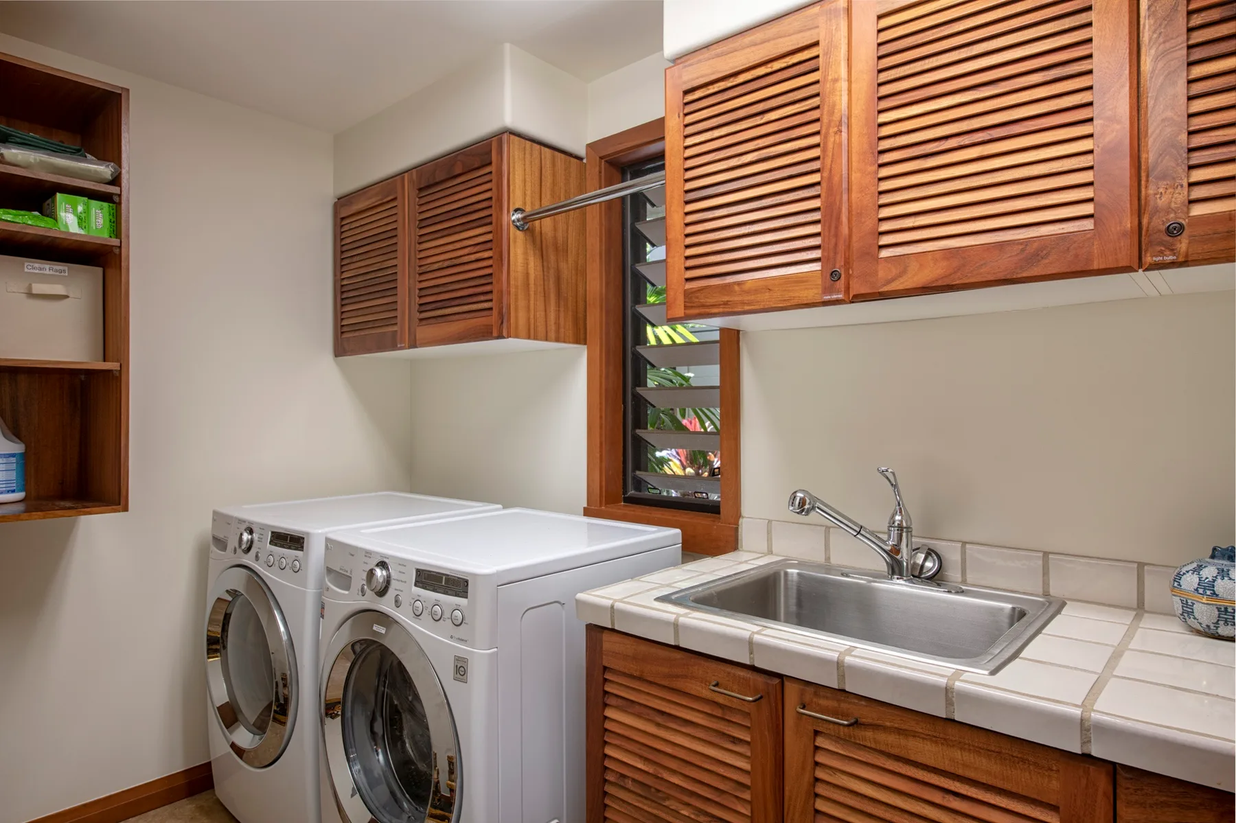 A laundry room with two washing machines and a utility sink beneath wooden cabinets.