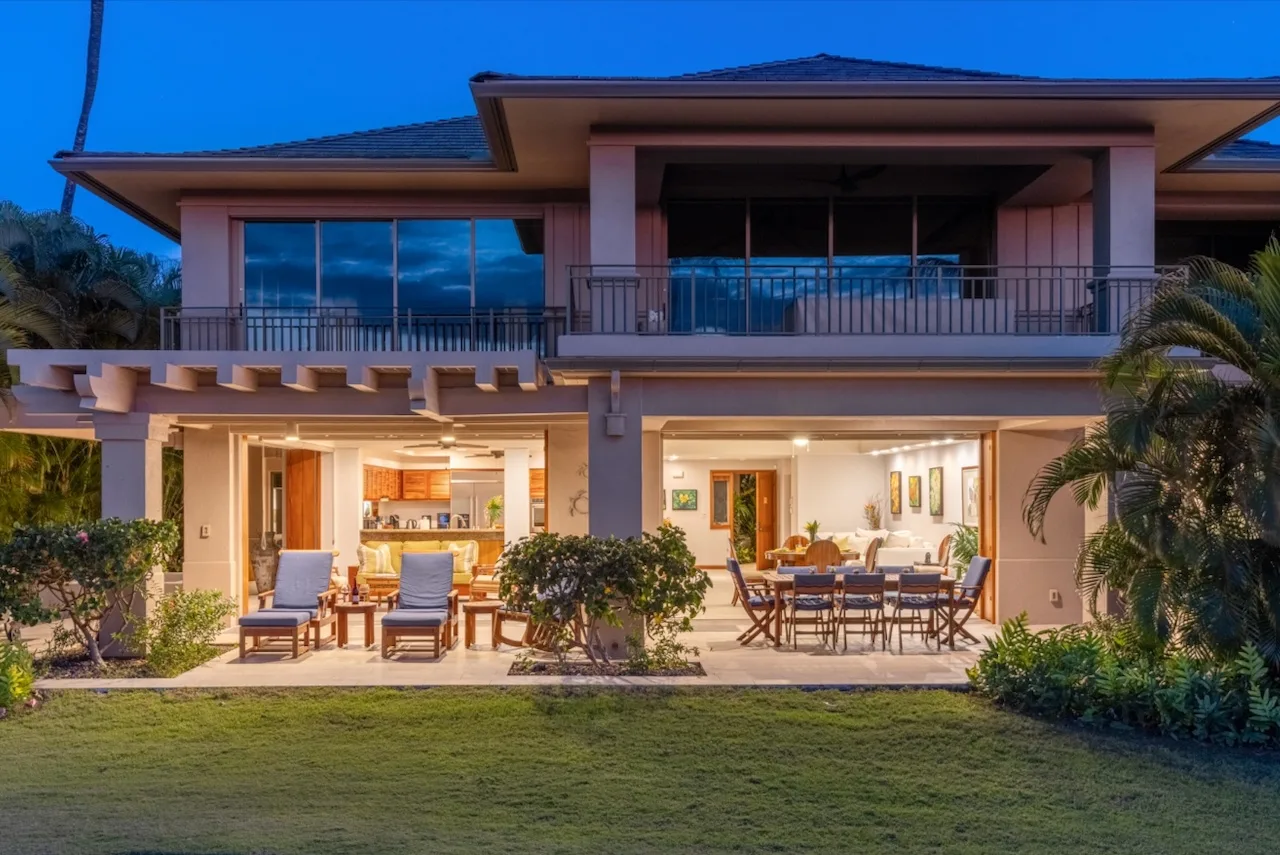 A two-story house opens onto a patio with outdoor seating and a dining table.