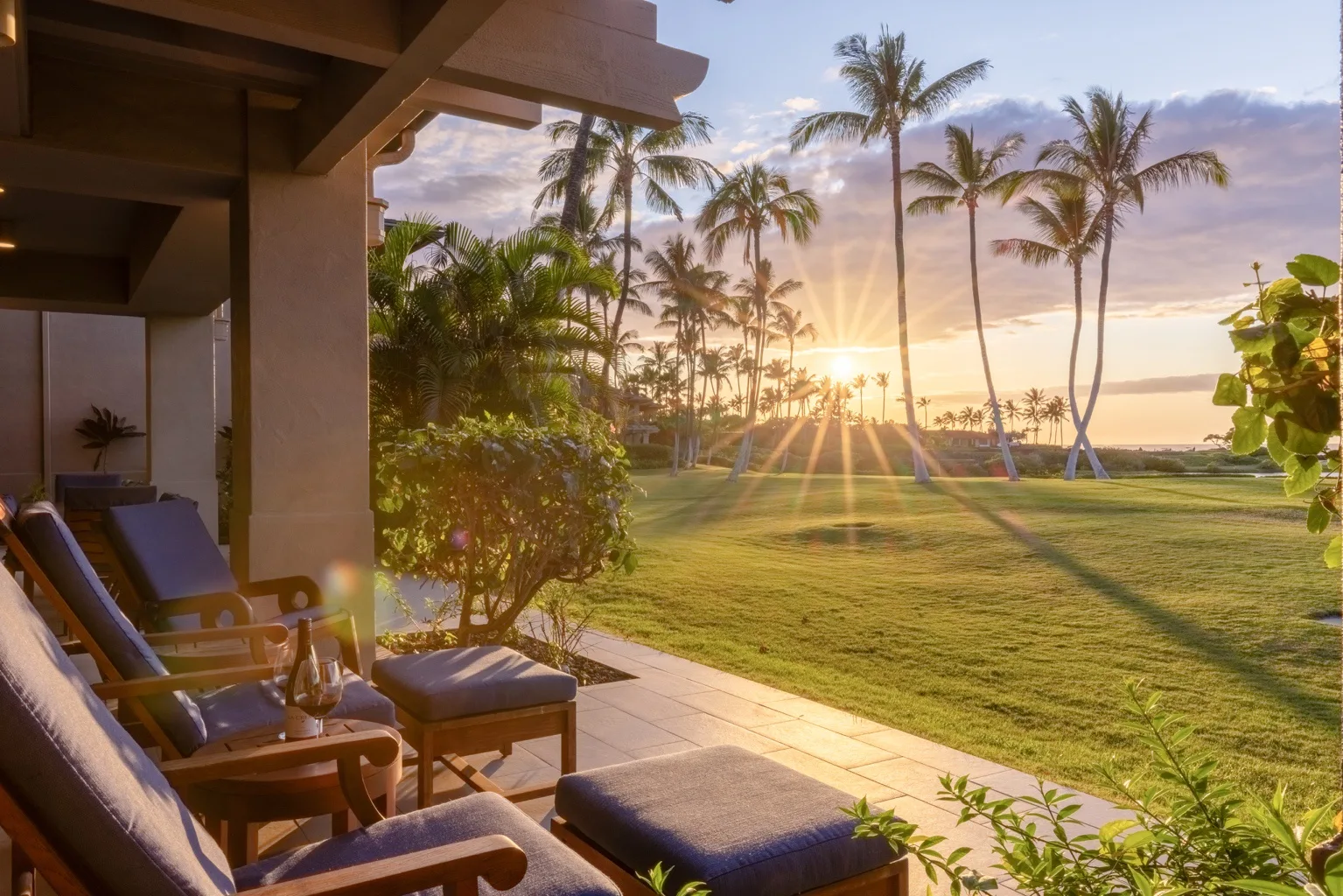 A tropical patio overlooks a grassy lawn and palm trees at sunset.