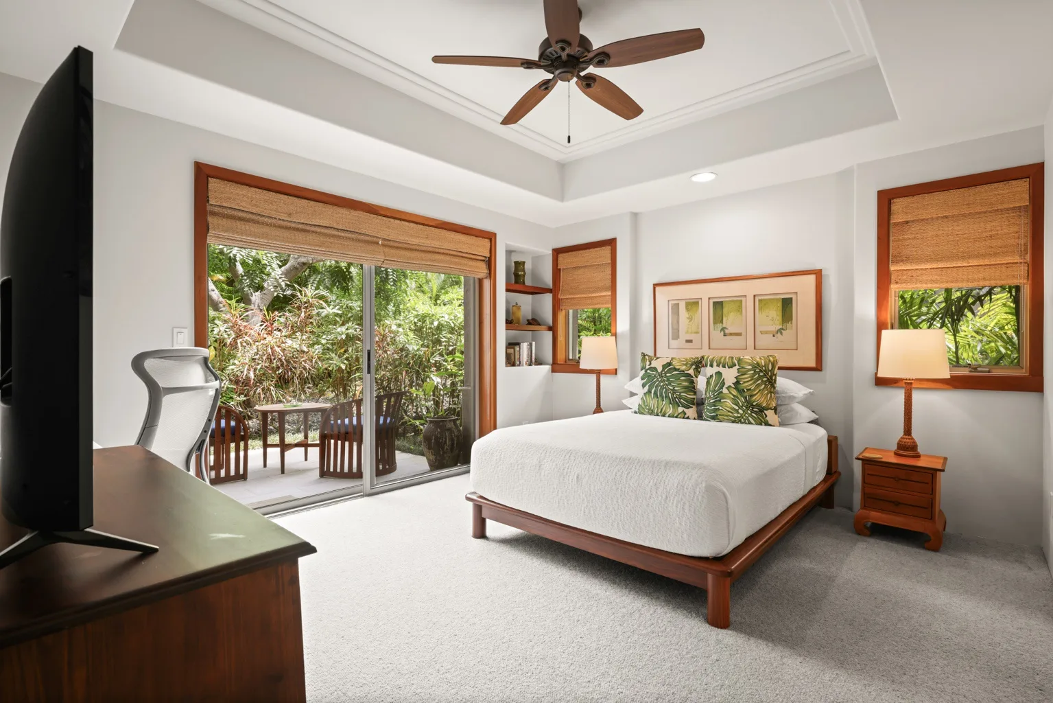 A bright bedroom with a bed, ceiling fan, and sliding glass doors opening to greenery.