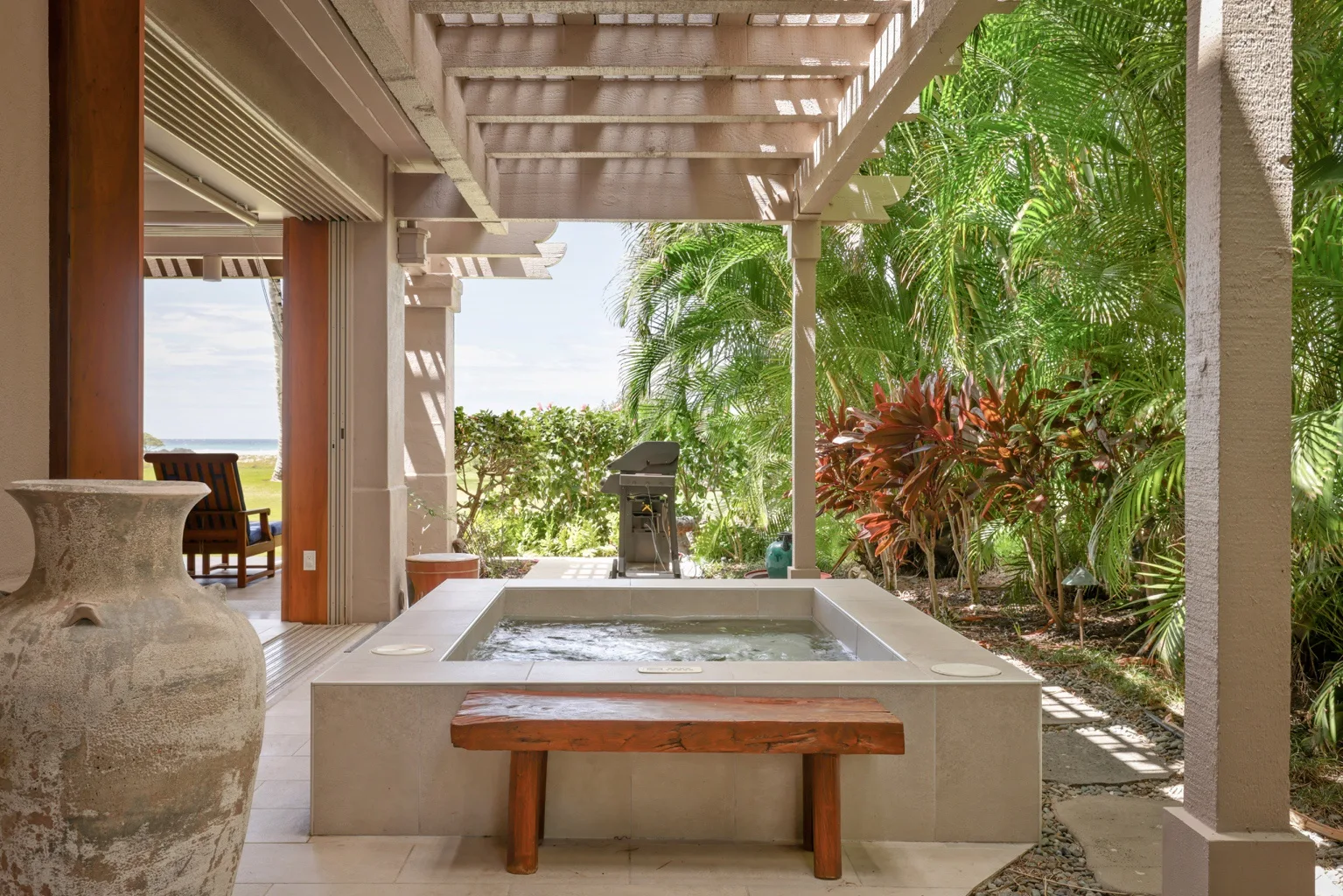 A covered outdoor patio features a raised soaking tub and lush tropical plants.