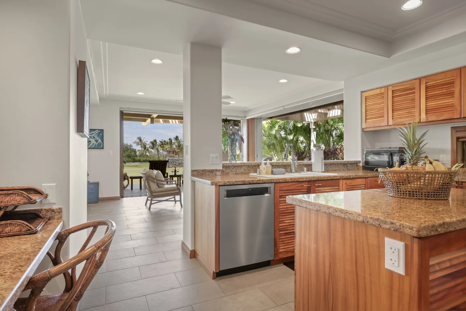 A bright kitchen with wooden cabinets, stone counters, and a view into the dining area.