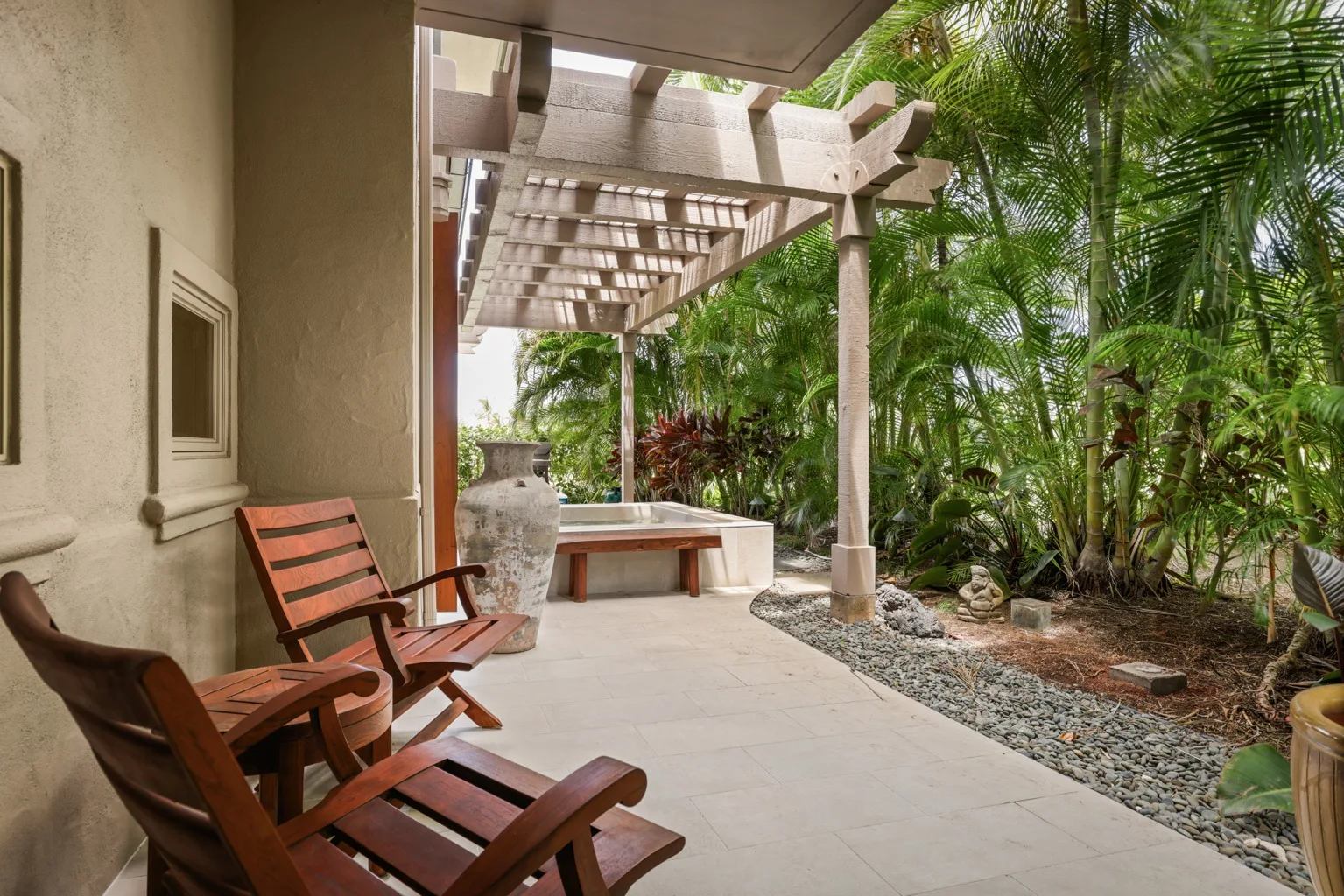 A covered patio with wooden seating beside a lush garden.