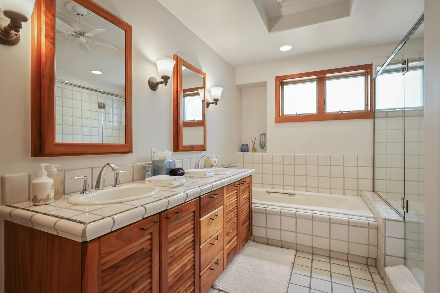 A tiled bathroom features a long vanity with a sink beside a bathtub.