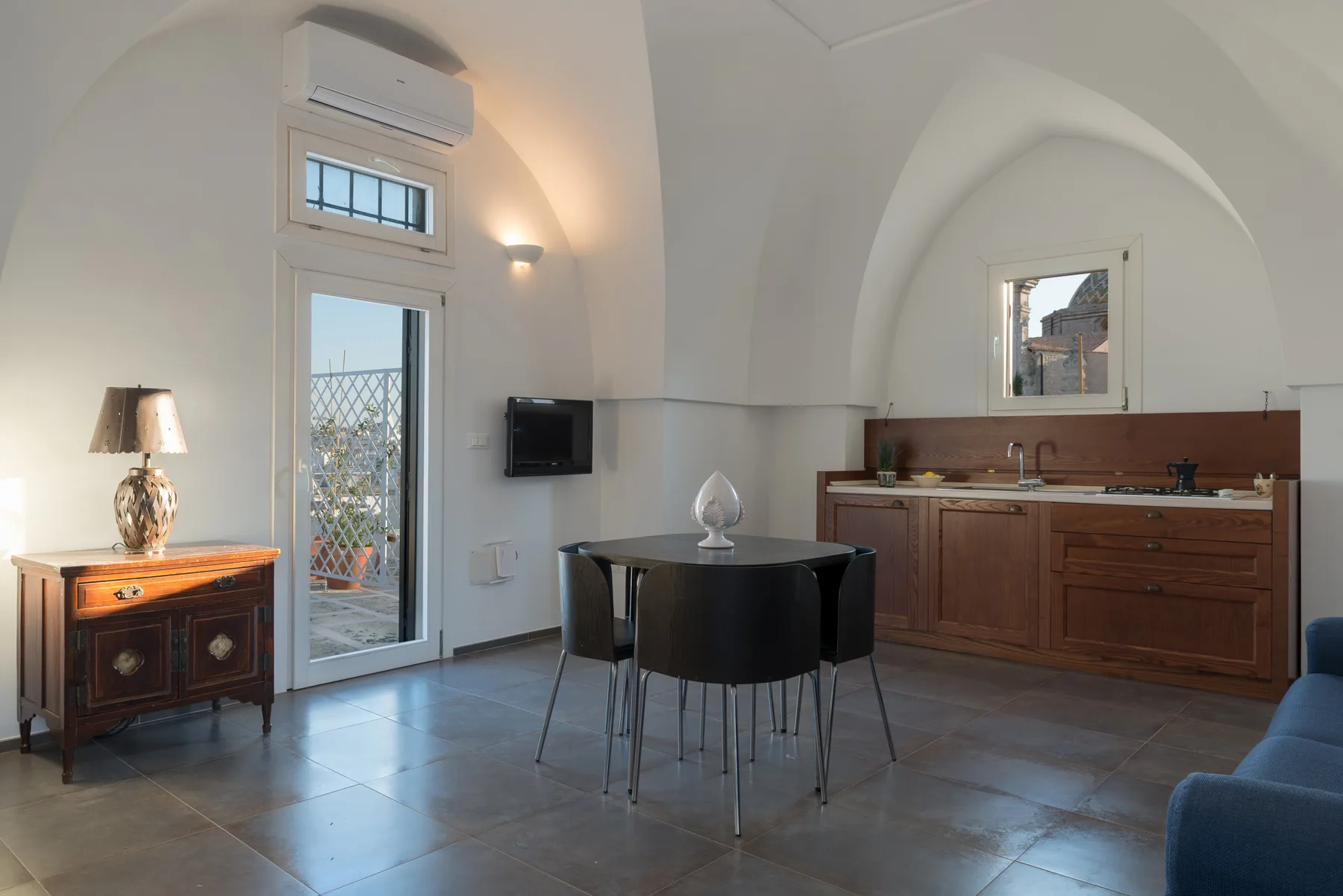 Zona de comedor y cocina con una mesa redonda y gabinetes de madera.