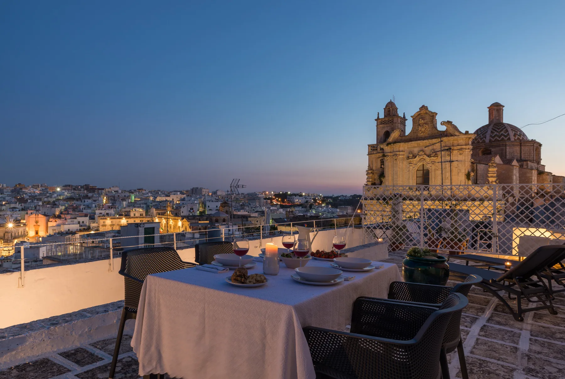 Una zona de comedor en una azotea ofrece vistas de la ciudad junto a un edificio iluminado.