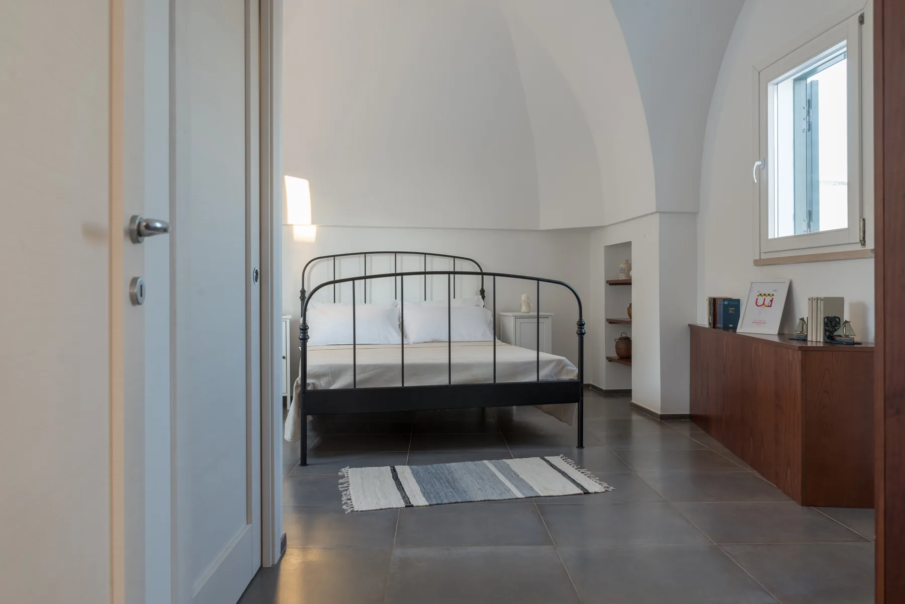 Un dormitorio con una cama de metal negro y un mueble bajo de madera.