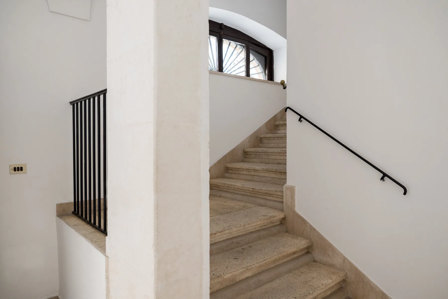 Una escalera interior con peldaños de piedra y un pasamanos negro en la pared.