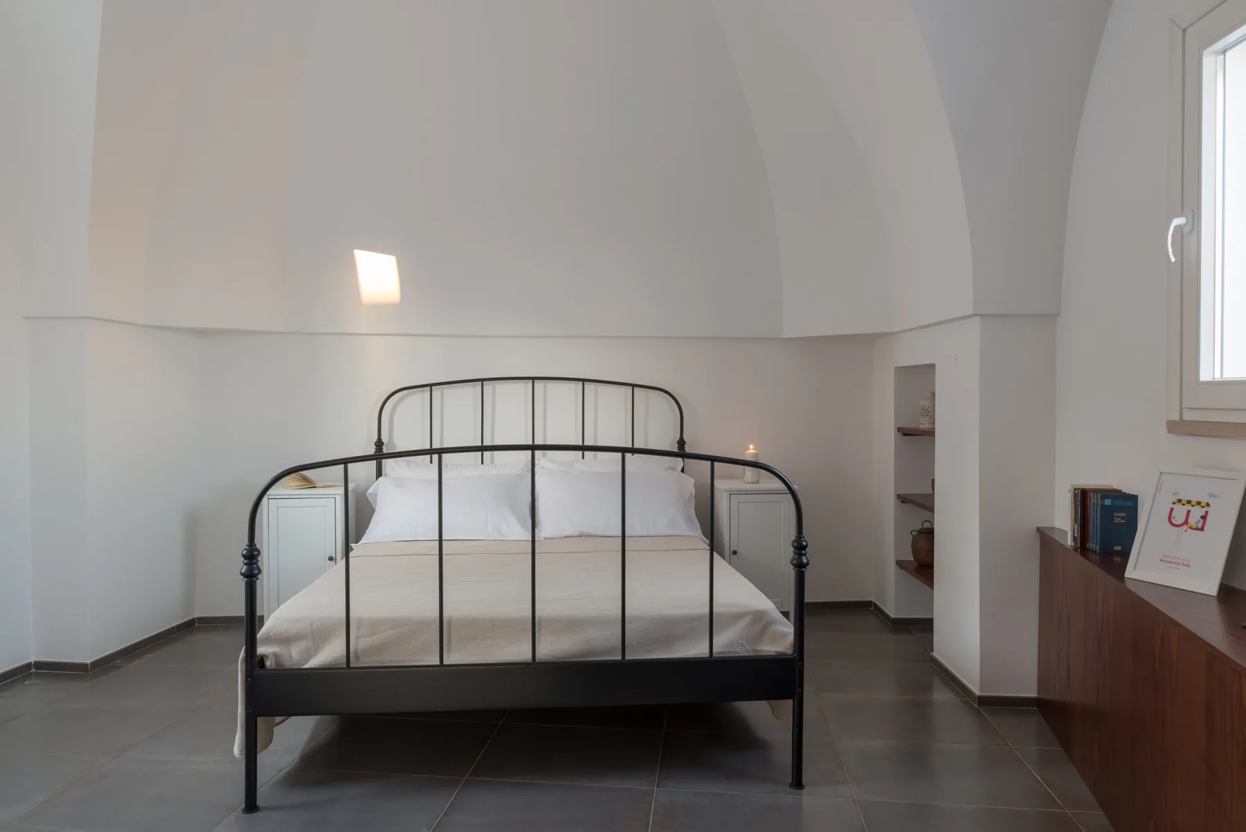 Un dormitorio con una cama de metal negro, ropa de cama blanca y techo curvo.