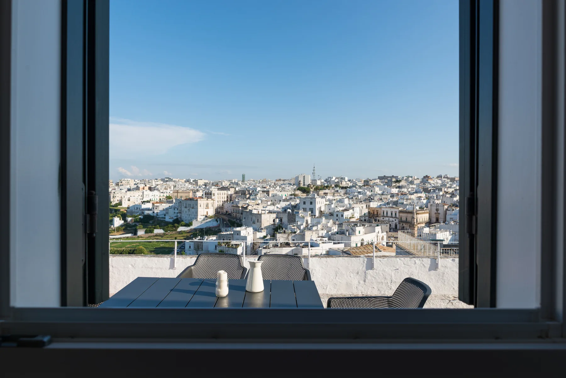 Vista de la ciudad desde una ventana abierta, con una mesa pequeña y asientos en primer plano.