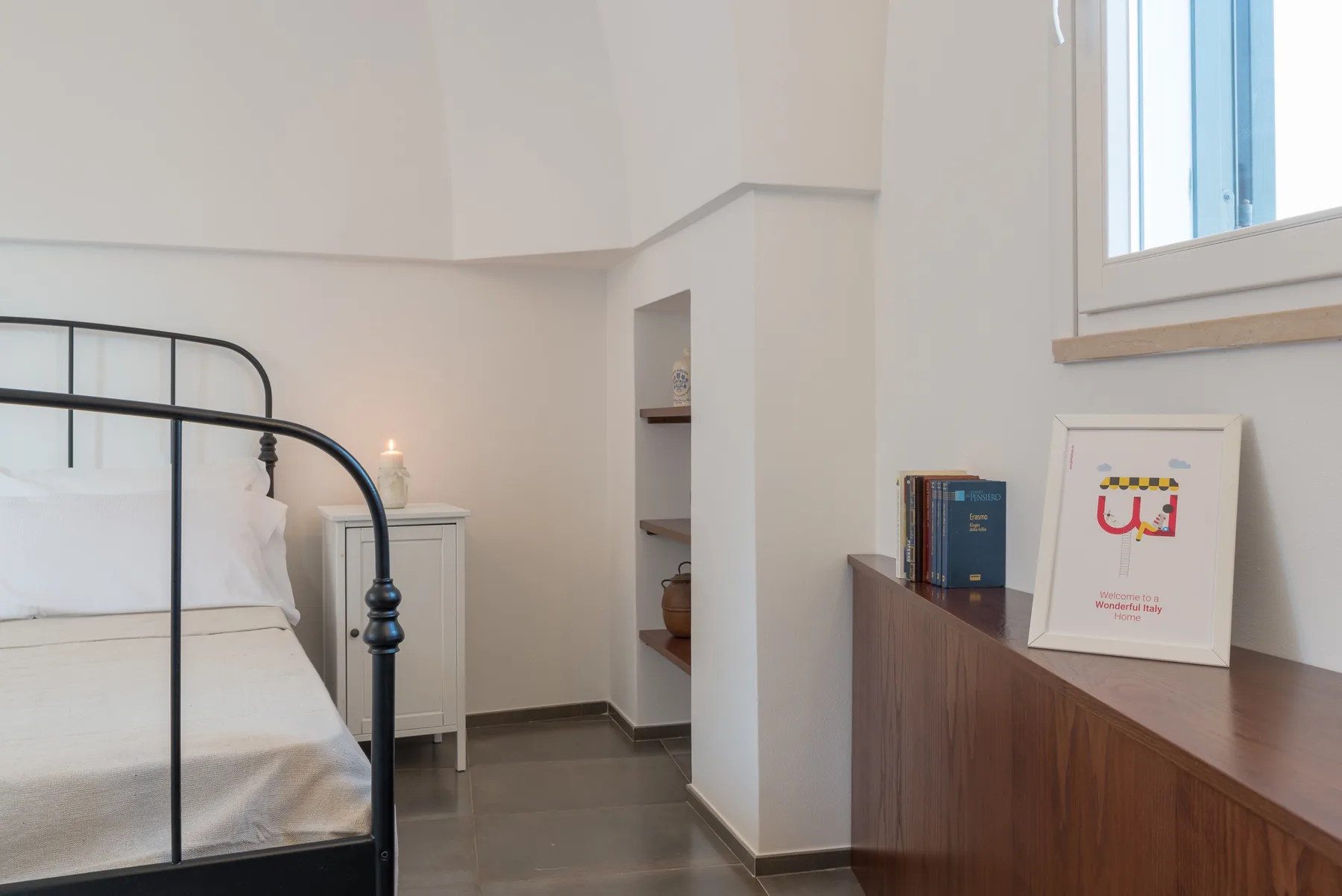 Un dormitorio con una cama de metal negro, un pequeño armario y una cómoda de madera.