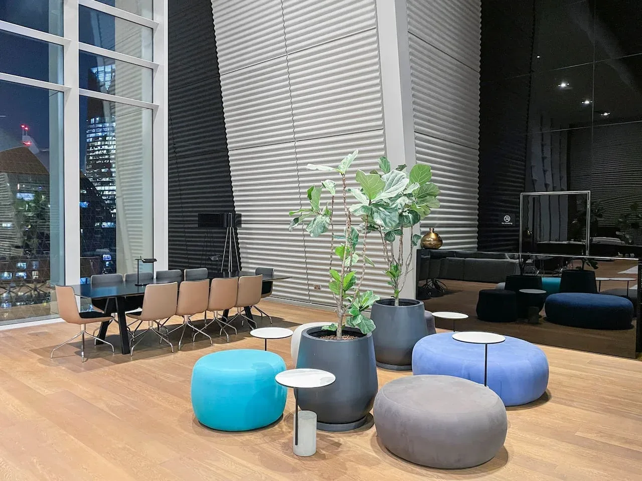 Una sala moderna con una mesa larga, asientos y grandes ventanales con vistas a las luces de la ciudad.