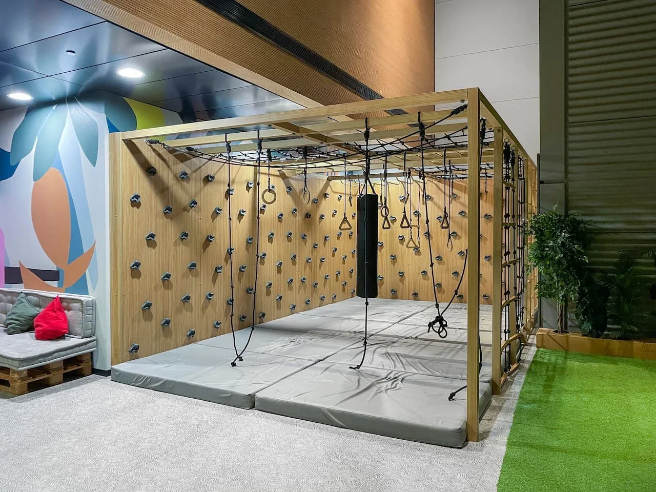 Una zona de escalada interior tiene una pared de madera con presas de colores y cuerdas colgantes.