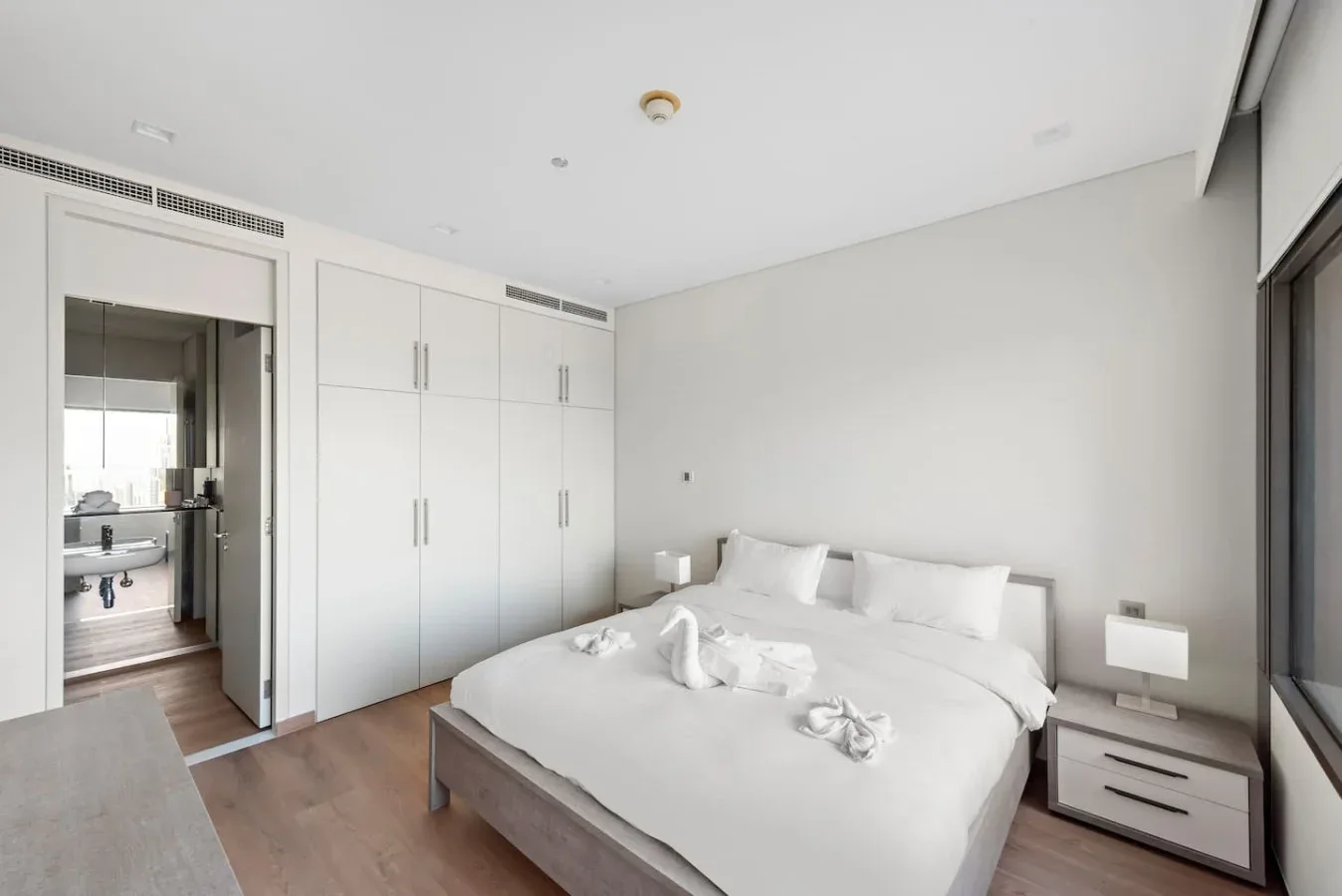 Un dormitorio luminoso con una cama ordenada y armarios empotrados blancos.