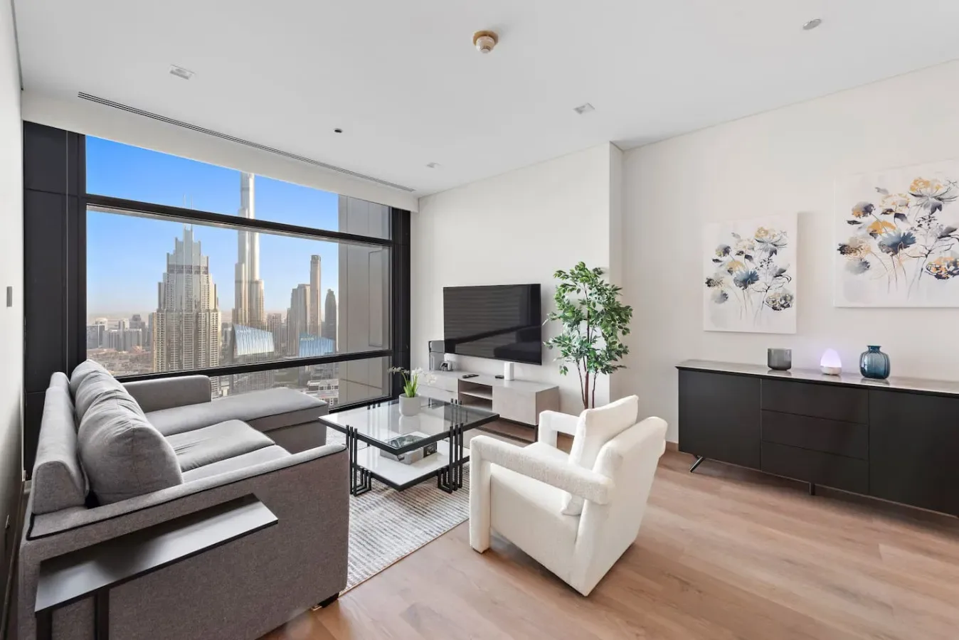 Una sala luminosa con asientos, un televisor y grandes ventanas con vistas a edificios de la ciudad.