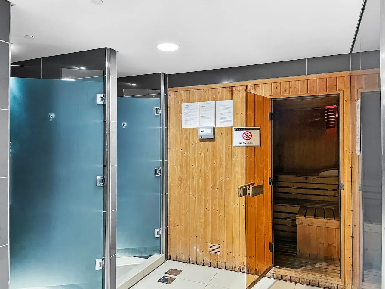 Una sala de sauna con una cabina de madera y duchas con mamparas de vidrio.