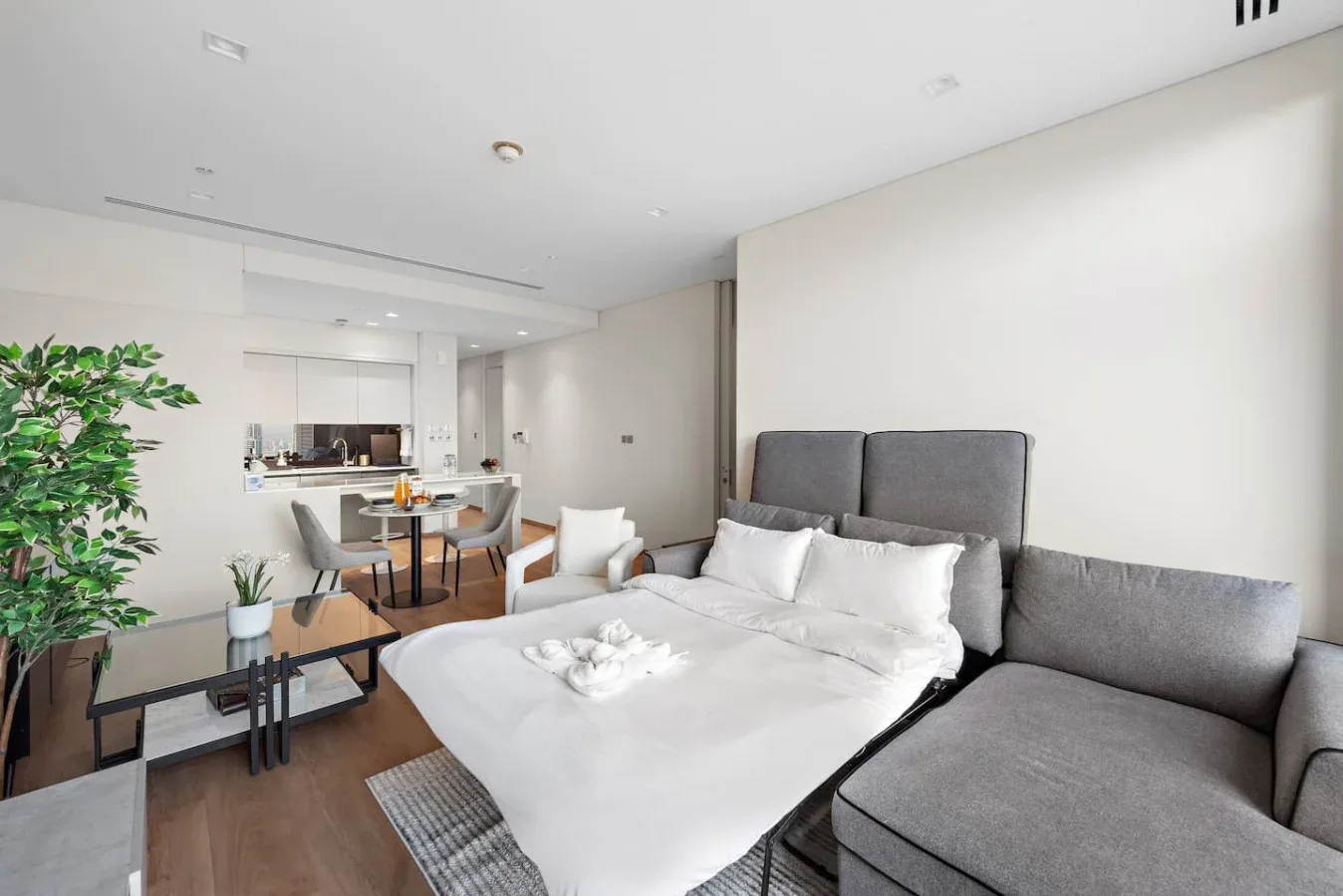 Un dormitorio con una cama grande y asientos grises junto a una zona de comedor.