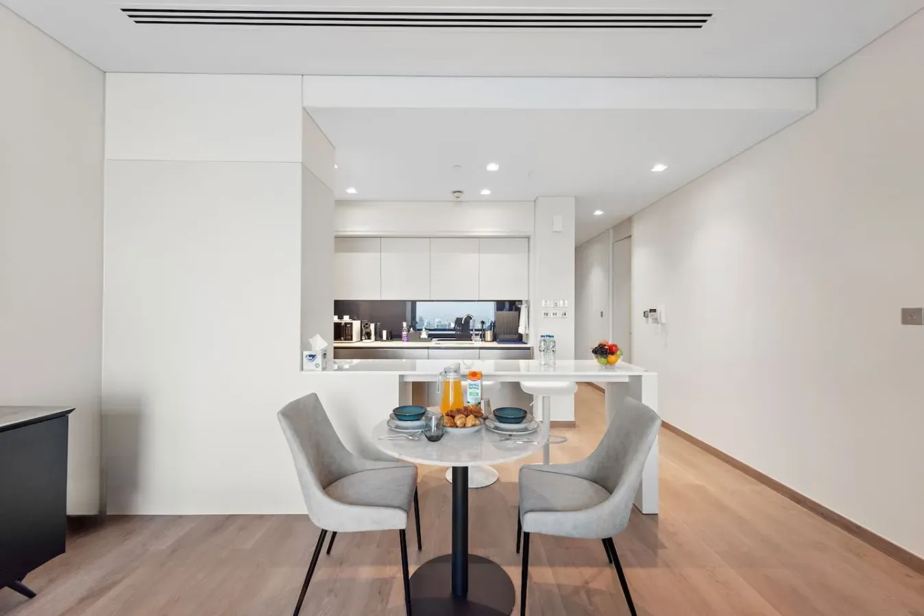 Un comedor luminoso con mesa y asientos da a una cocina abierta.