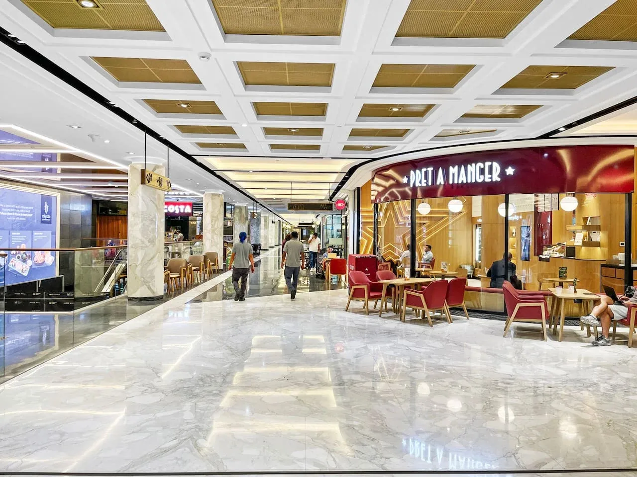 Pasillo de un centro comercial con tiendas y una zona de mesas de restaurante.