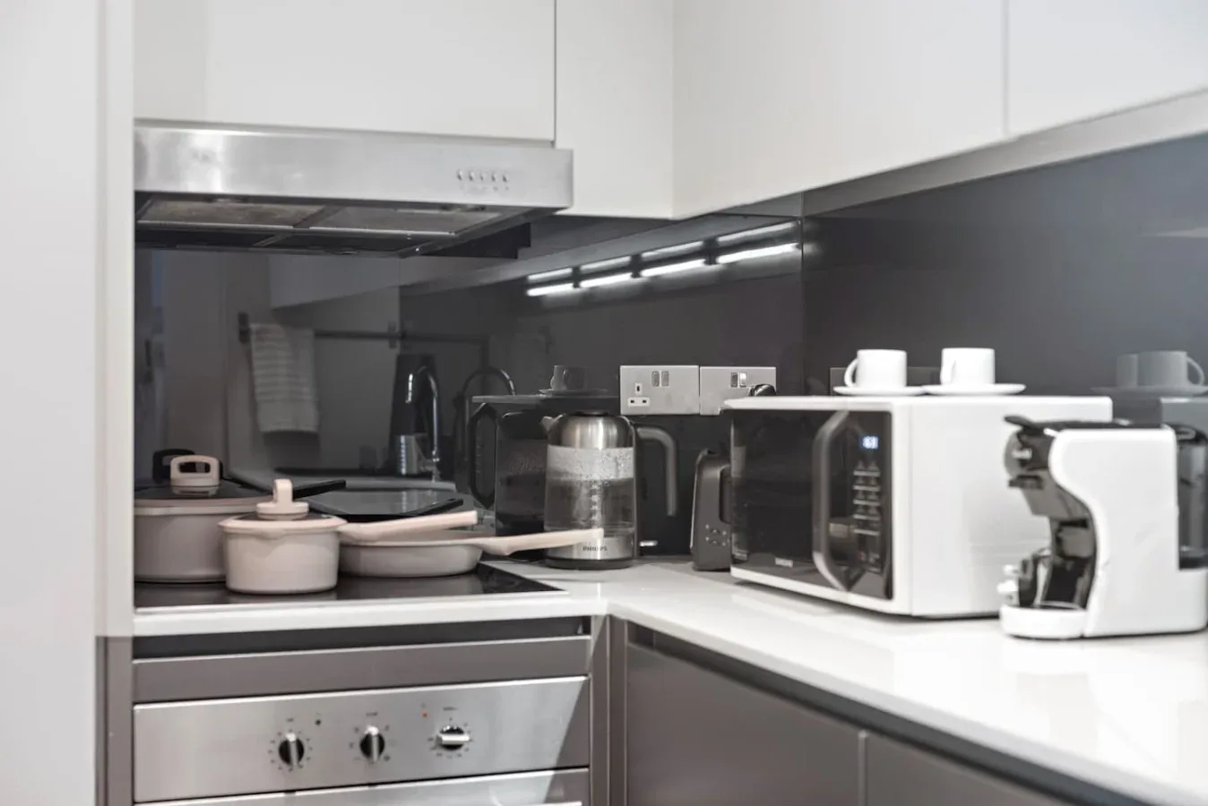 Una cocina compacta con gabinetes blancos, electrodomésticos sobre la encimera y utensilios de cocina.