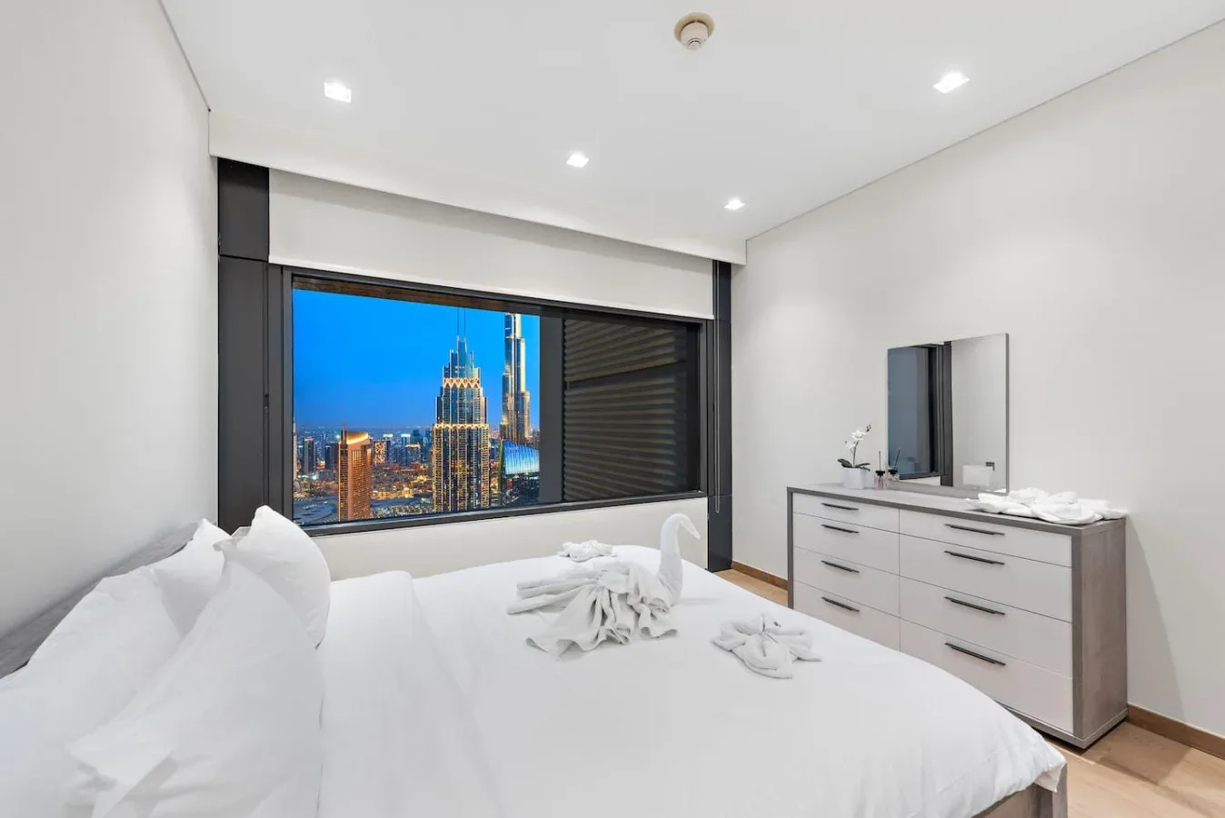 Un dormitorio luminoso con ropa de cama blanca y vistas a la ciudad por la ventana.