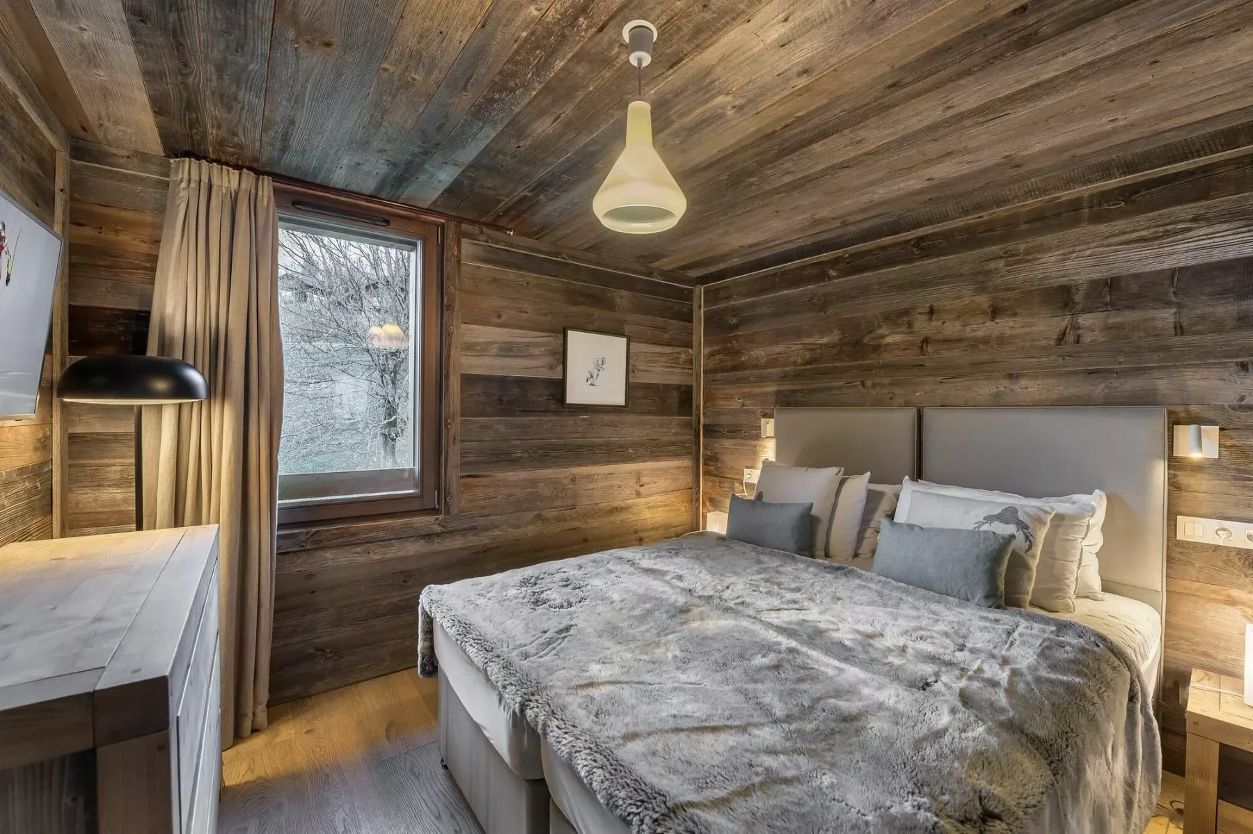 A bedroom with a bed, bedside tables, and a curtained window.