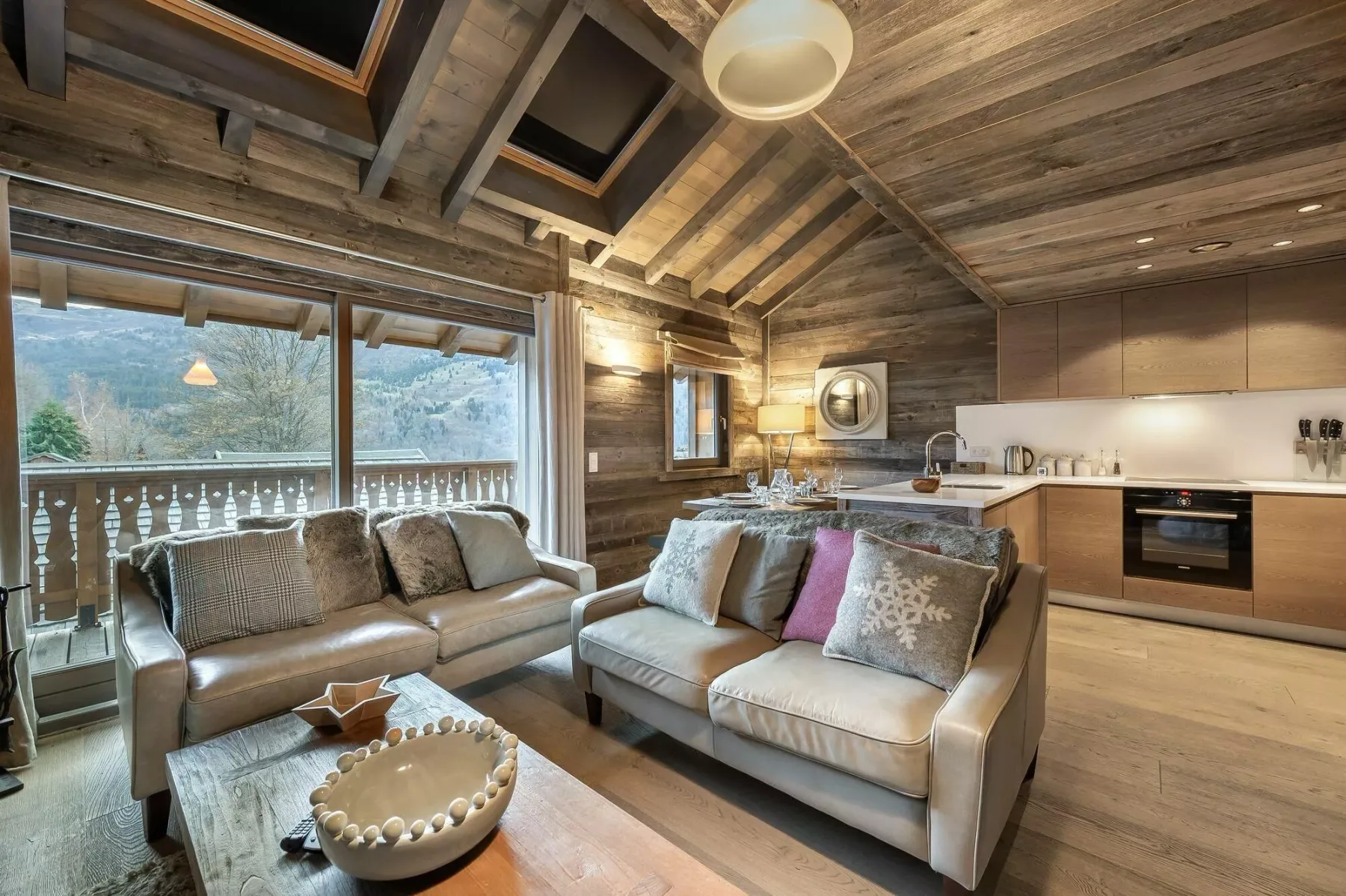 A wood-paneled living room with seating beside large windows and an open kitchen.