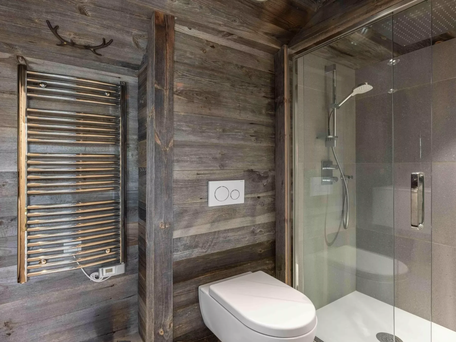 A bathroom with a glass shower, toilet, and wall-mounted towel warmer.