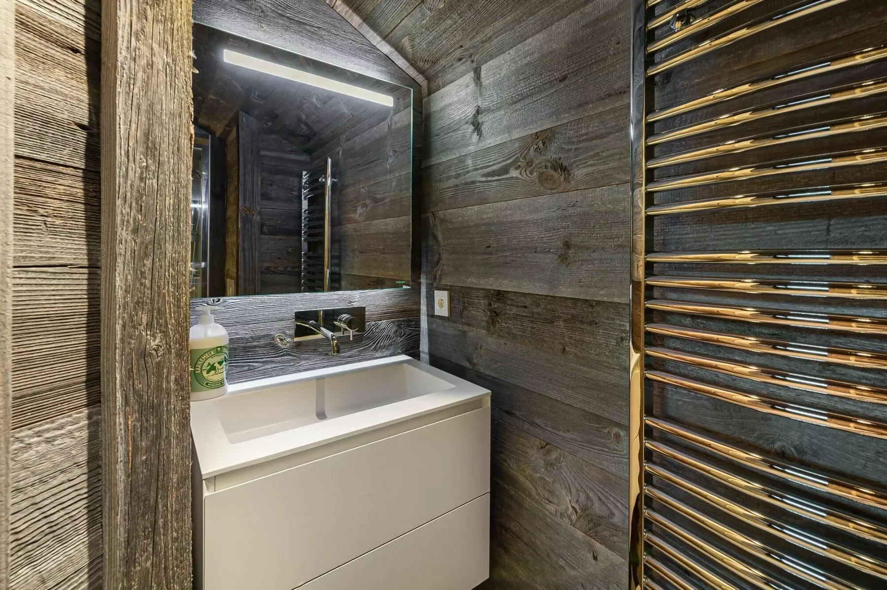 A bathroom vanity with a sink sits beneath a large mirror, beside a wall-mounted towel warmer.