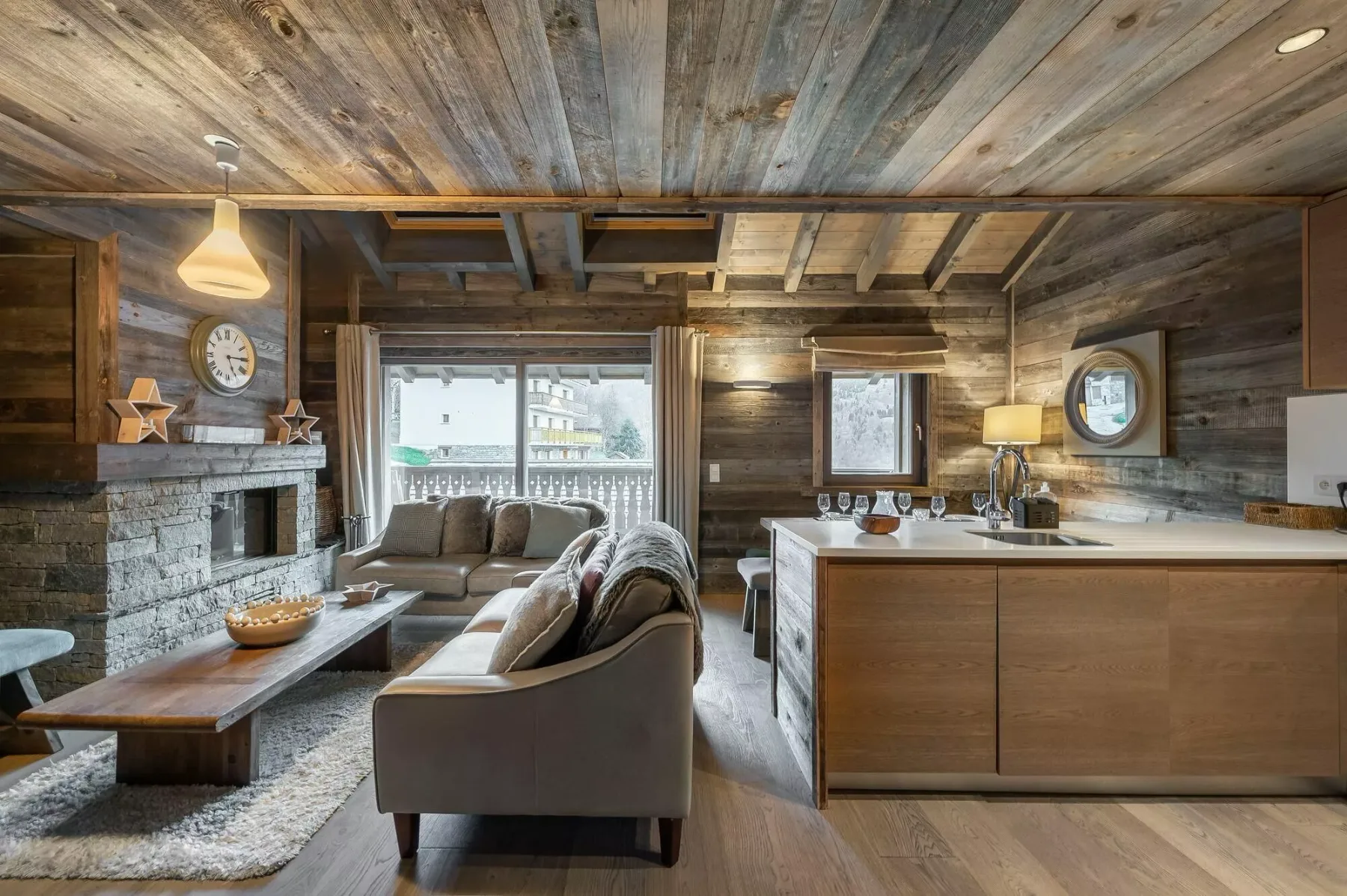 A rustic living room with a stone fireplace, seating, and a kitchen island.