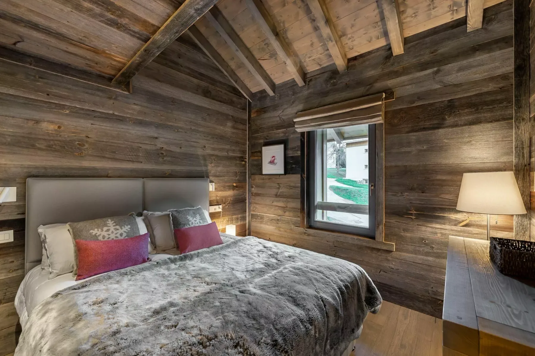 A bedroom with a bed beneath a sloped wooden ceiling and a window.