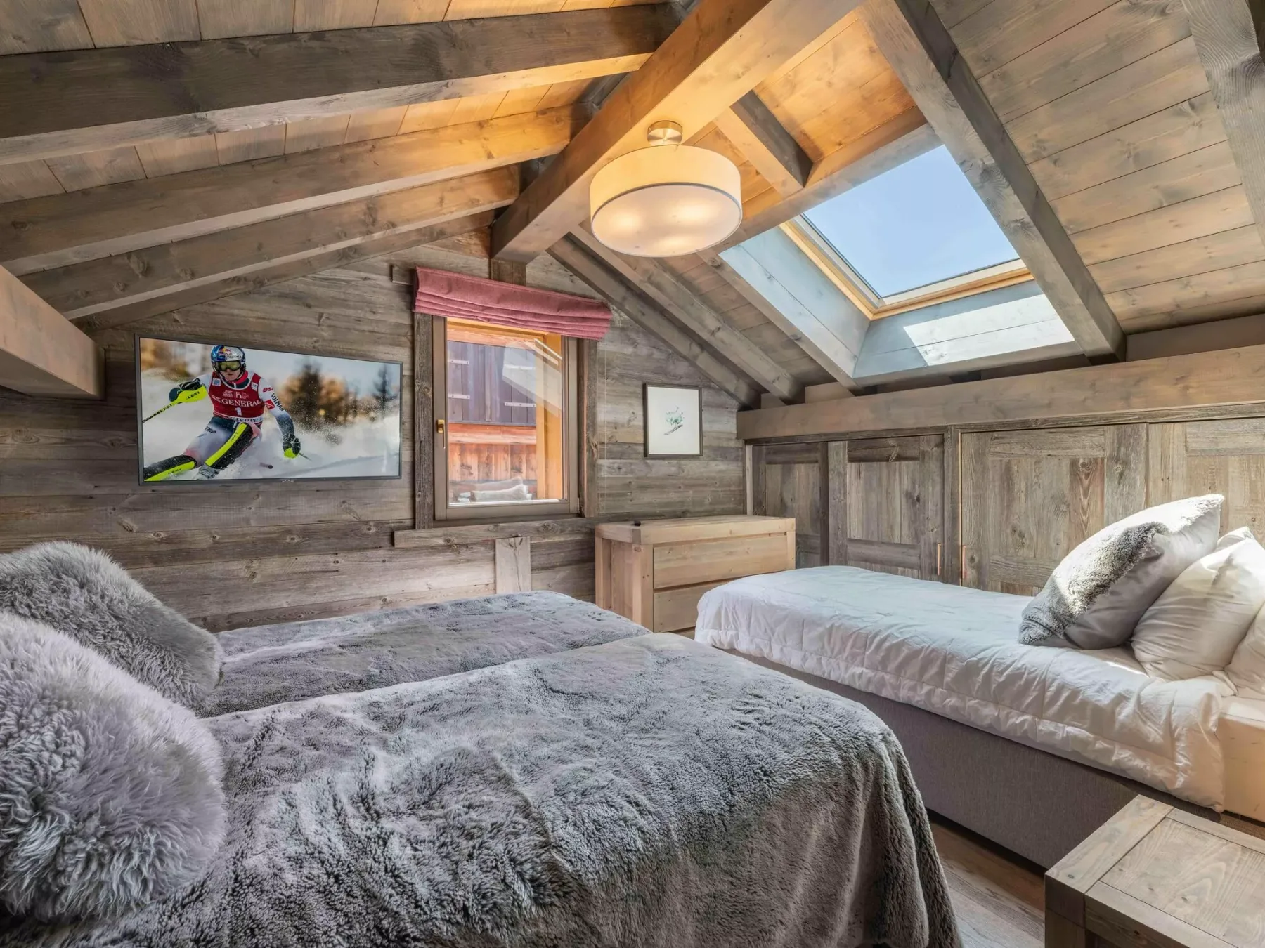 A rustic attic bedroom with two beds beneath a sloped timber ceiling and skylight.